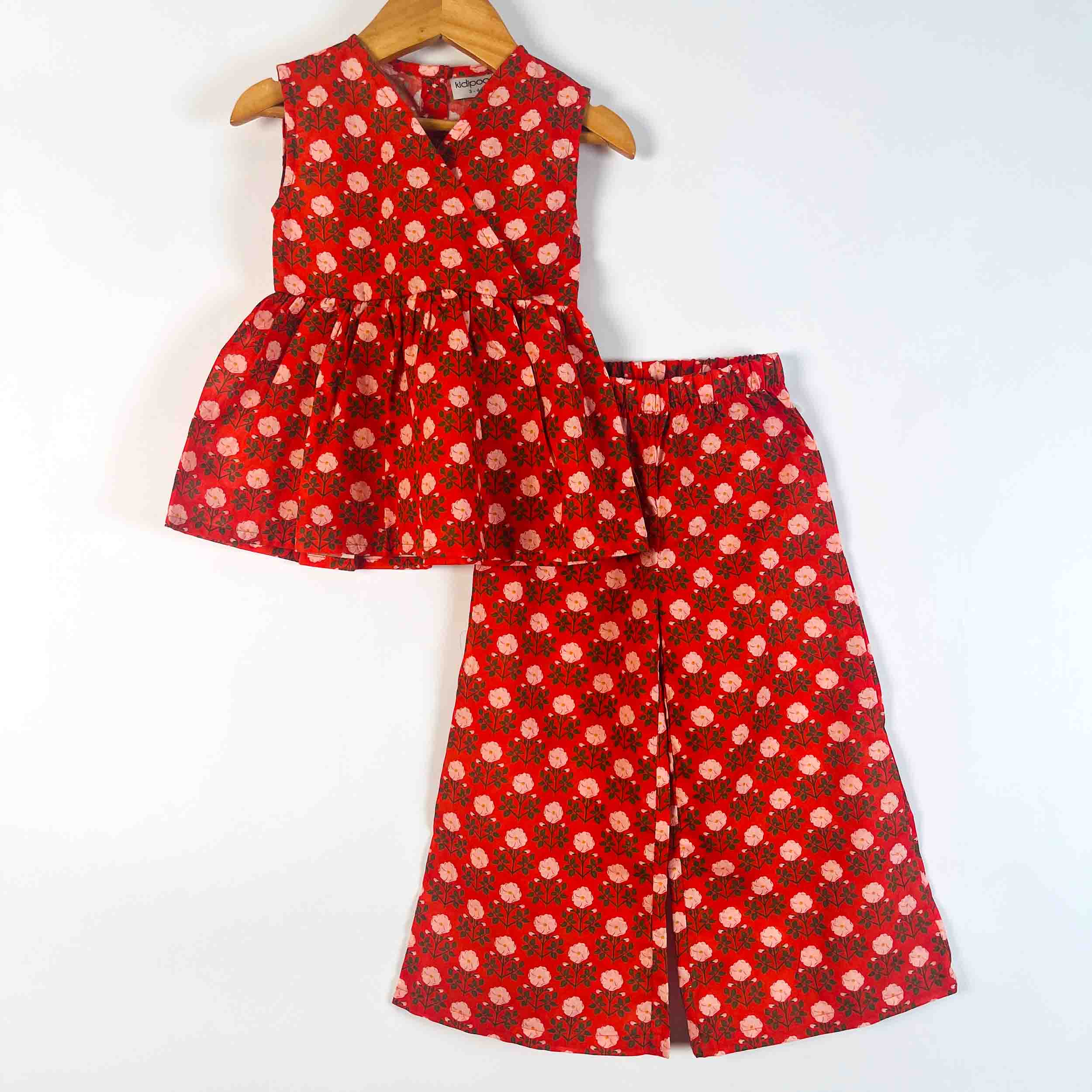 A two-piece children's outfit set consisting of a sleeveless red top with a white floral print and matching red wide-leg pants, displayed on wooden hangers against a plain white background.