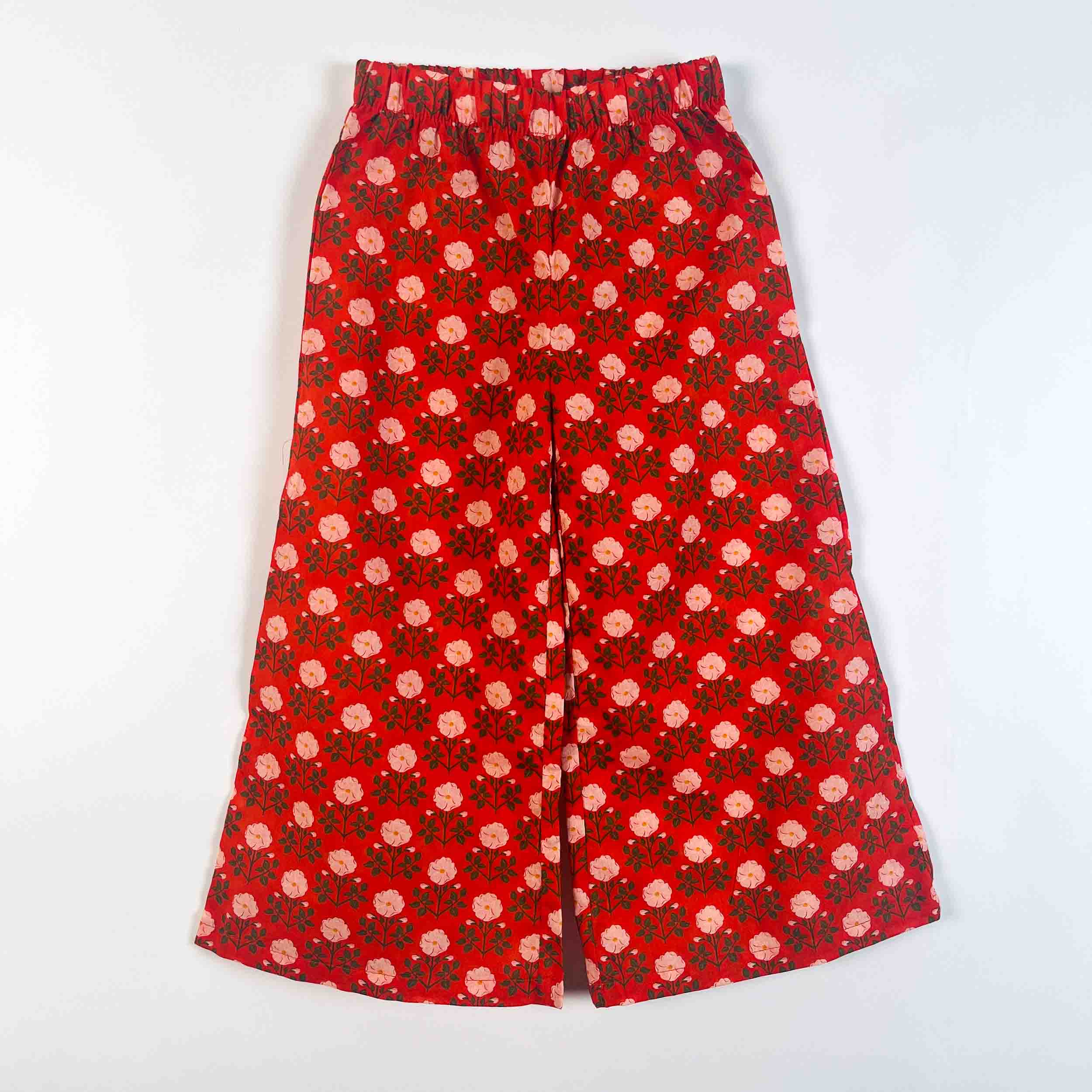 Red wide-leg pants with an all-over pink and green floral print, featuring an elastic waistband, laid flat against a white background.
