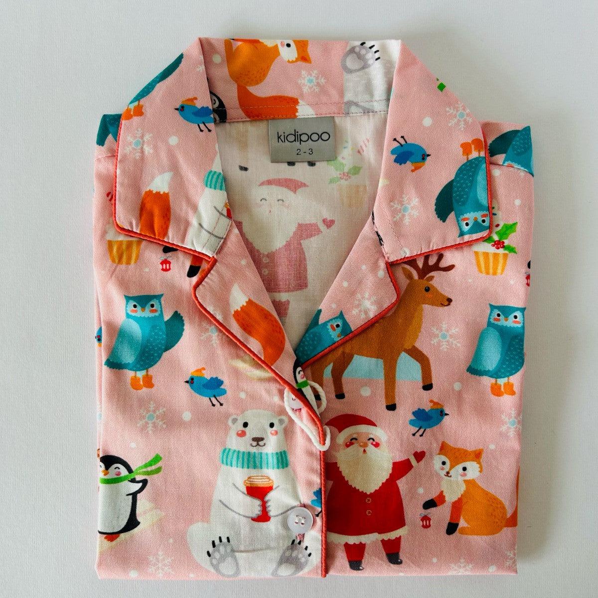 A pink night suit with a Christmas theme, featuring illustrations of Santa, reindeer, and snowflakes.