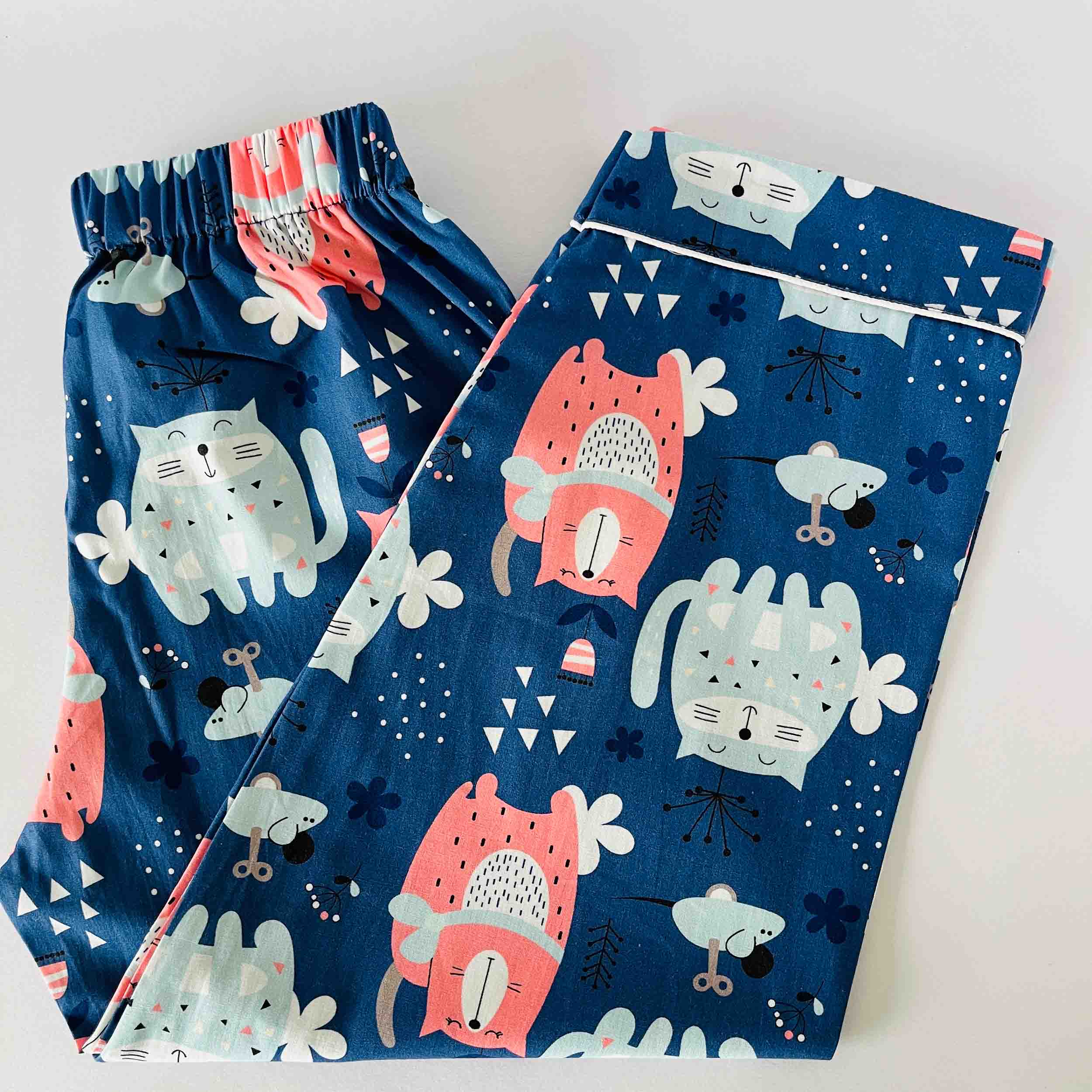 Pair of blue pajama pants with cartoon cat design on a white background