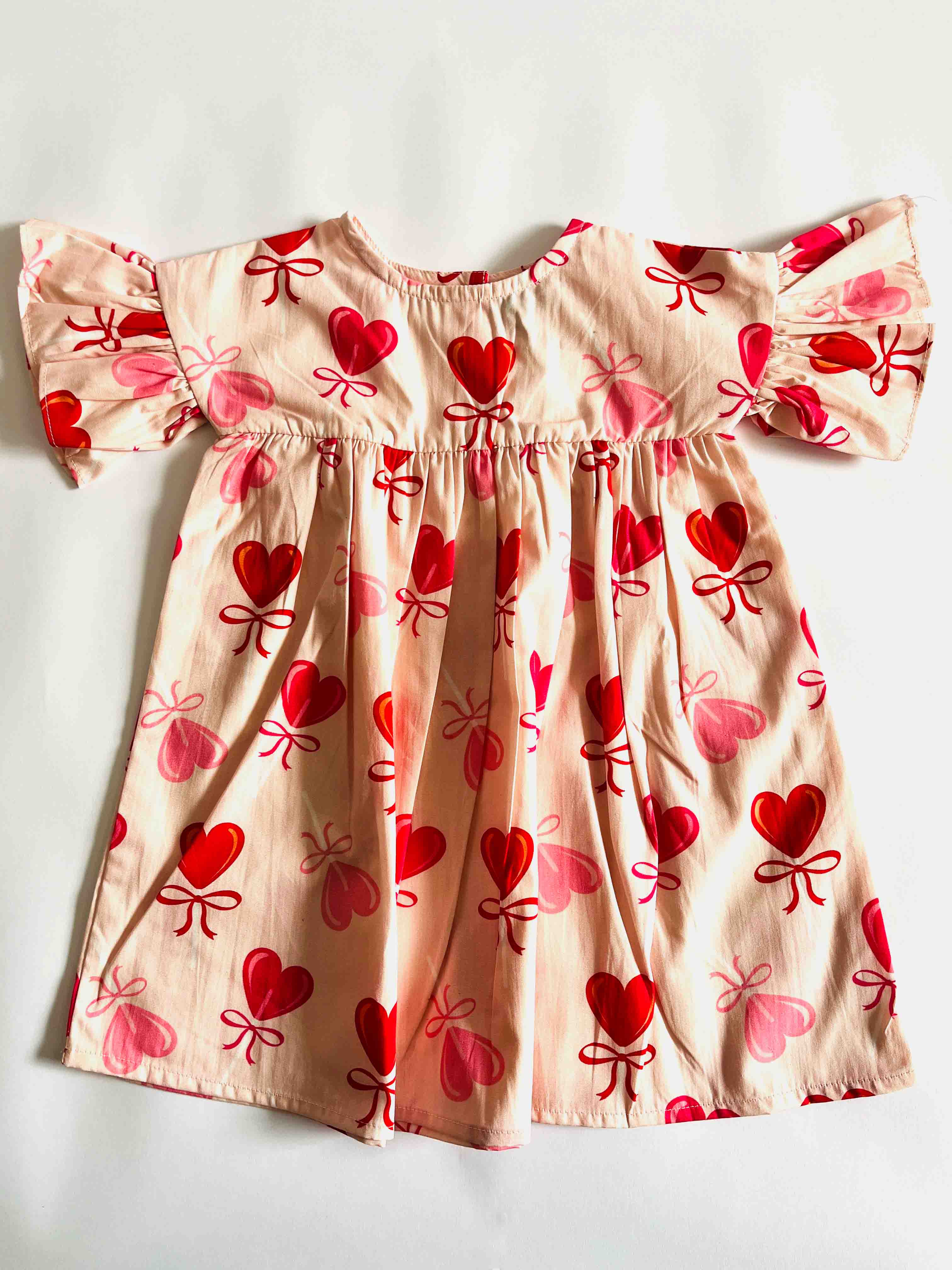 Children's dress with red heart and bow pattern on a plain background