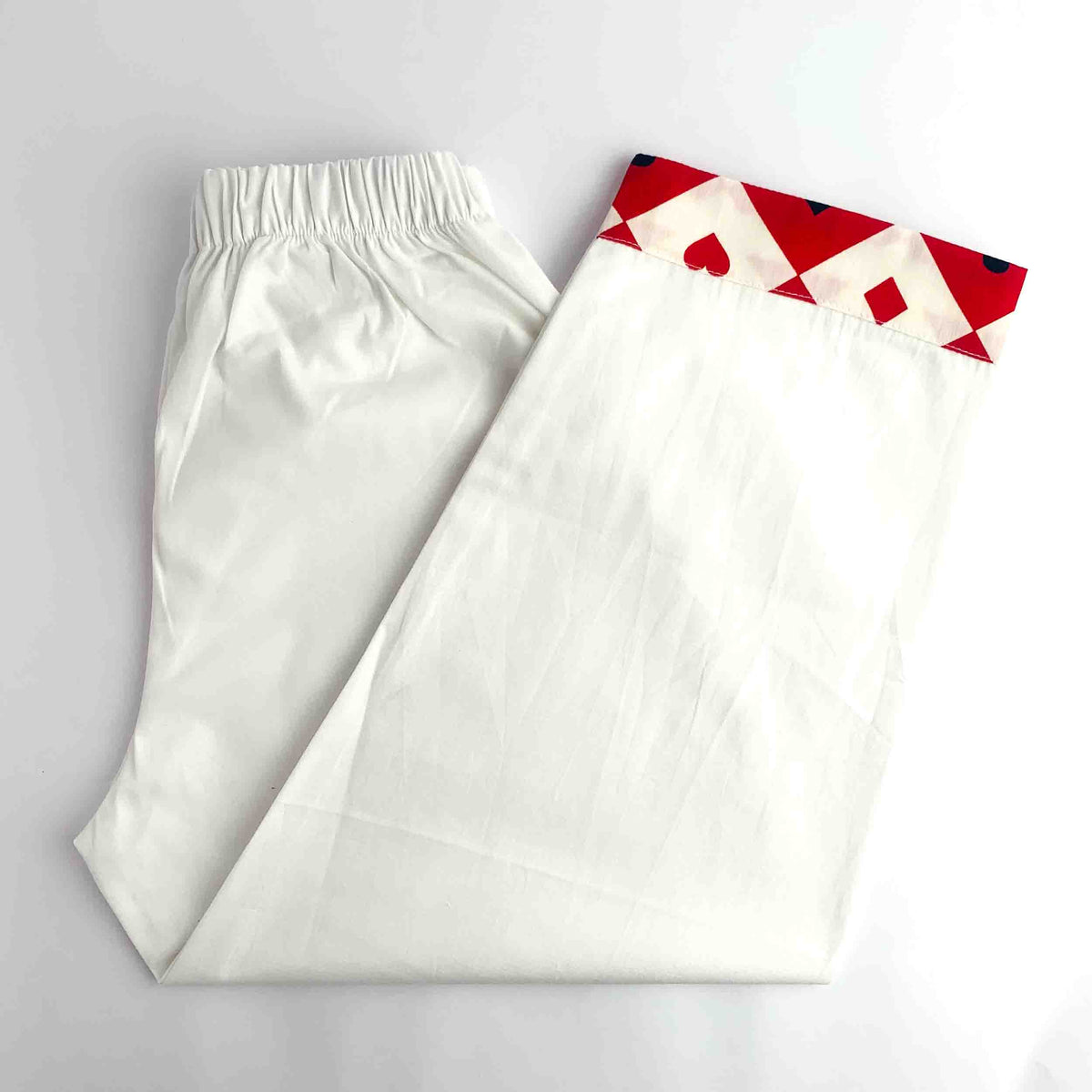 White elastic-waist pants with a red and white geometric print at the bottom, folded on a white background