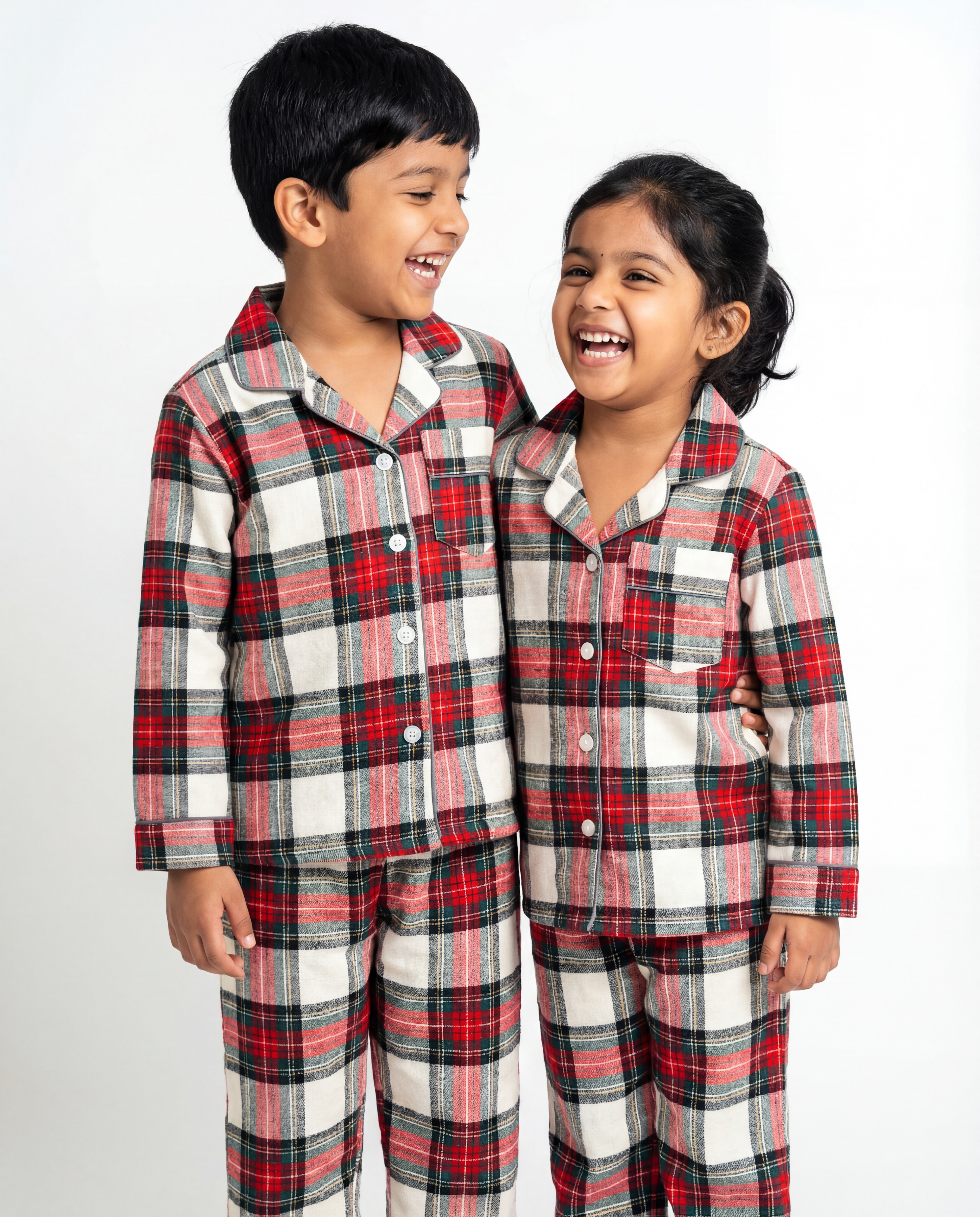 Two children wearing red and gray plaid pajamas on a white background