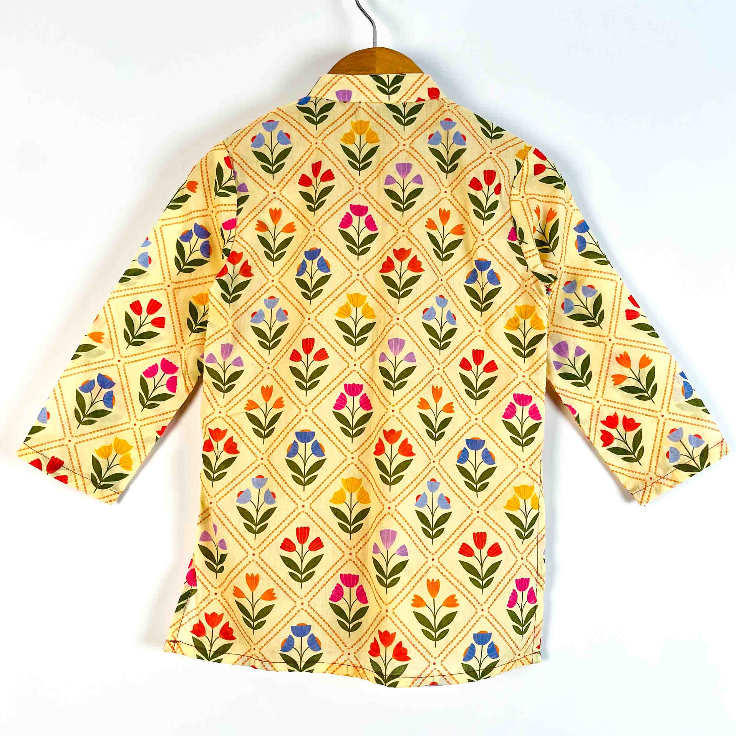 A cream-colored cotton shirt with a colorful floral and diamond pattern, hanging on a wooden hanger against a white background.