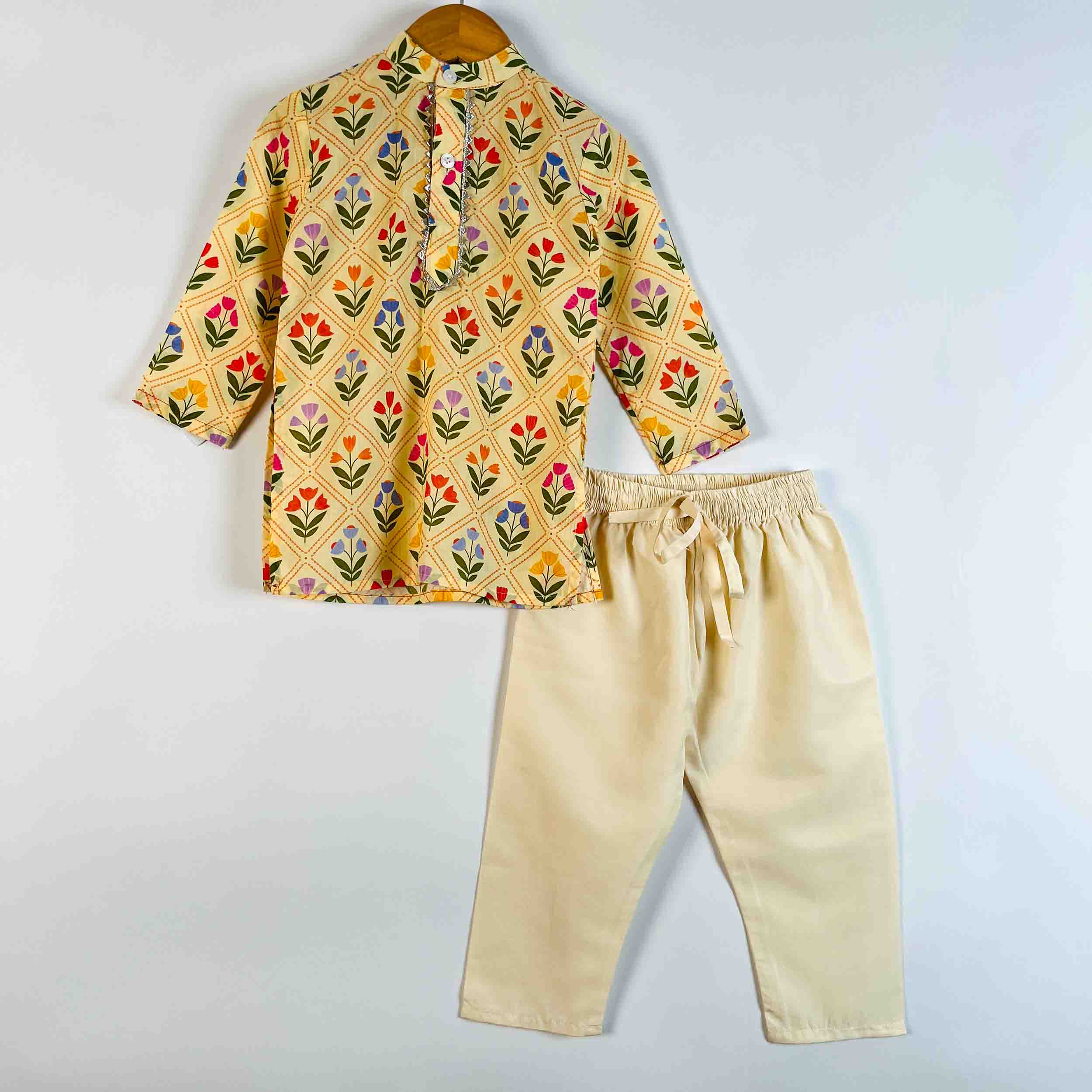 A children's two-piece outfit set consisting of a yellow patterned kurta with colorful floral motifs and cream-colored pants, displayed on a light gray background.